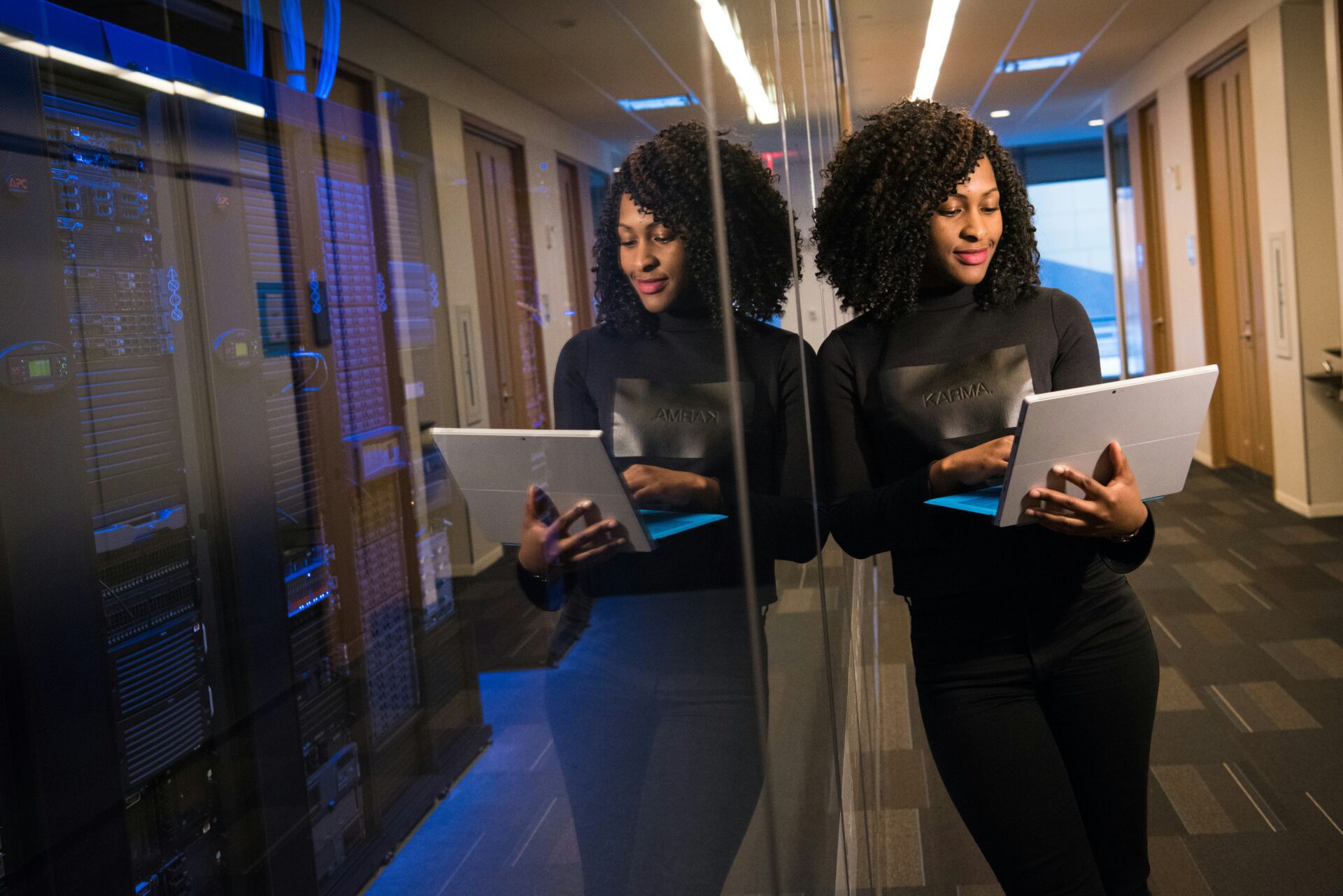 An IT administrator works on her laptop while standing next to servers.